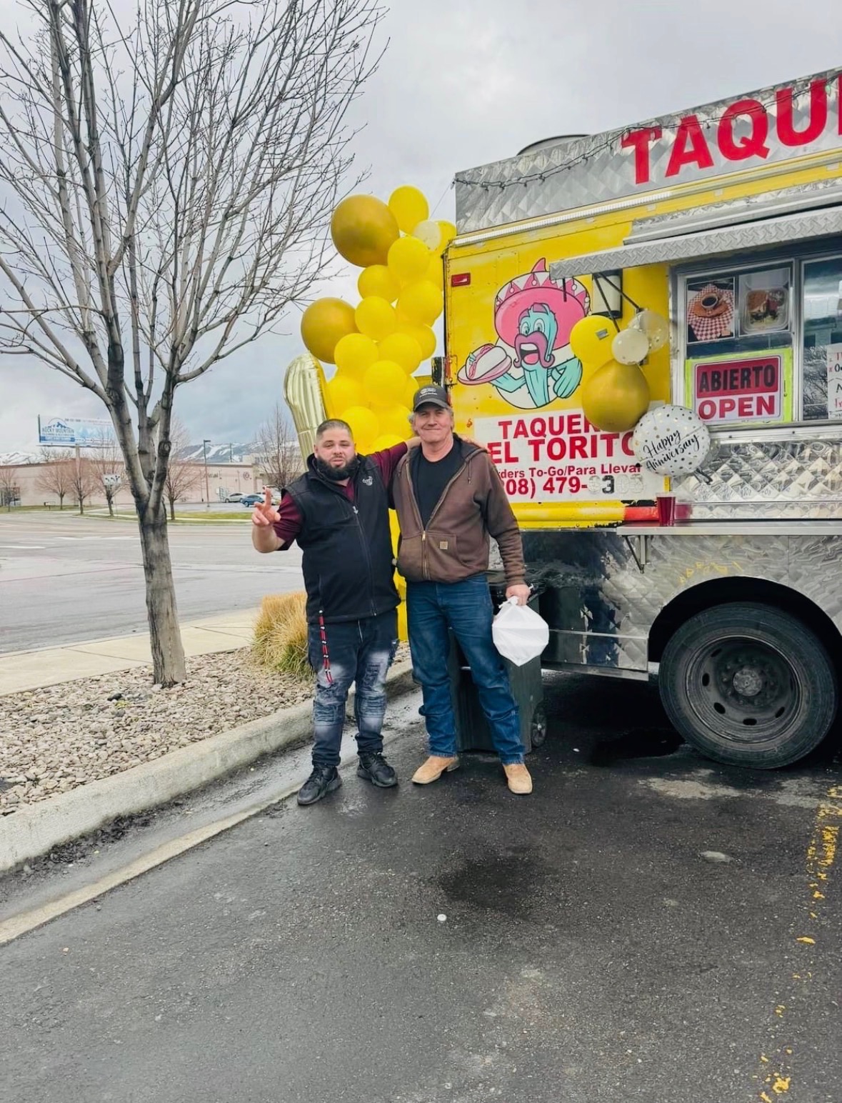 Two customers smiling in front of the decorated Taquería El Torito truck