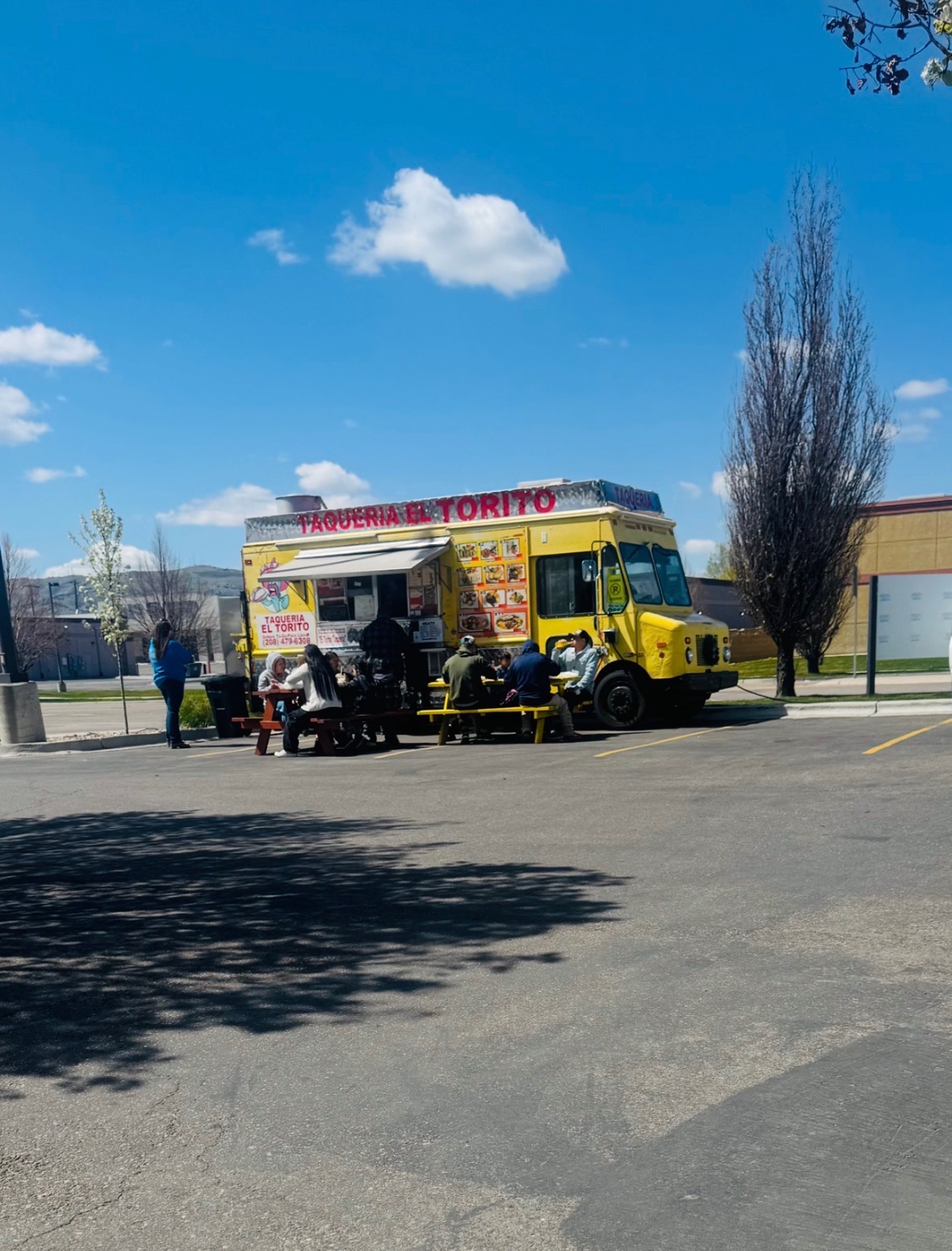 Customers eating at picnic tables beside the yellow El Torito truck on a sunny day